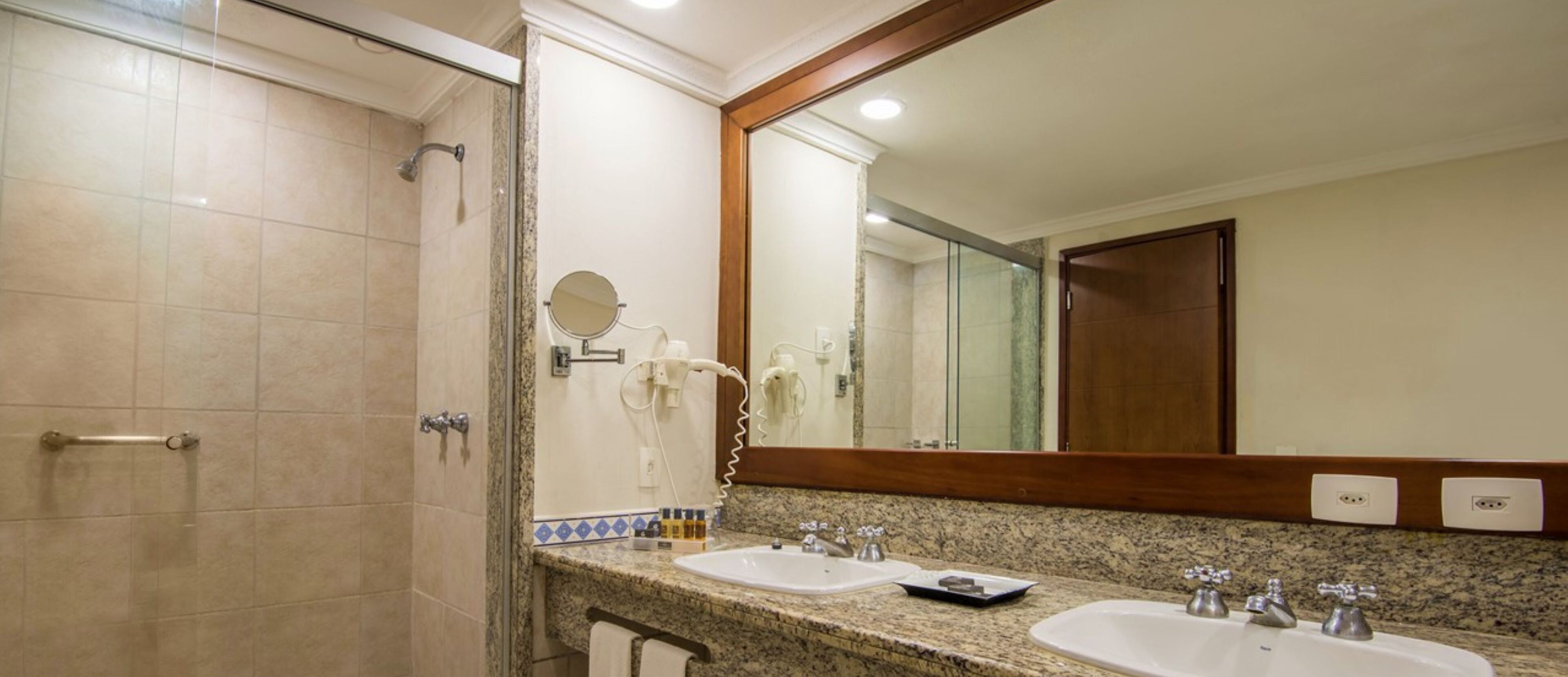 A bathroom with two sinks, a shower, and a large mirror.
