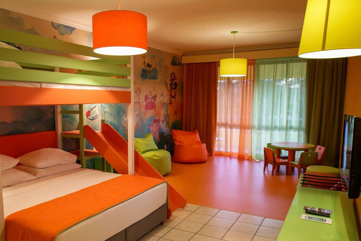 A brightly colored hotel room with bunk beds, a desk, and a small dining area.
