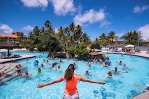 A swimming pool with multiple people, surrounded by palm trees and a clear blue sky. - Vila Galé Cabo – All Inclusive (Cabo de Santo Agostinho)