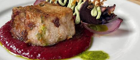 Ein Teller Essen mit Fleisch, Roter Bete und einer grünen Soße.