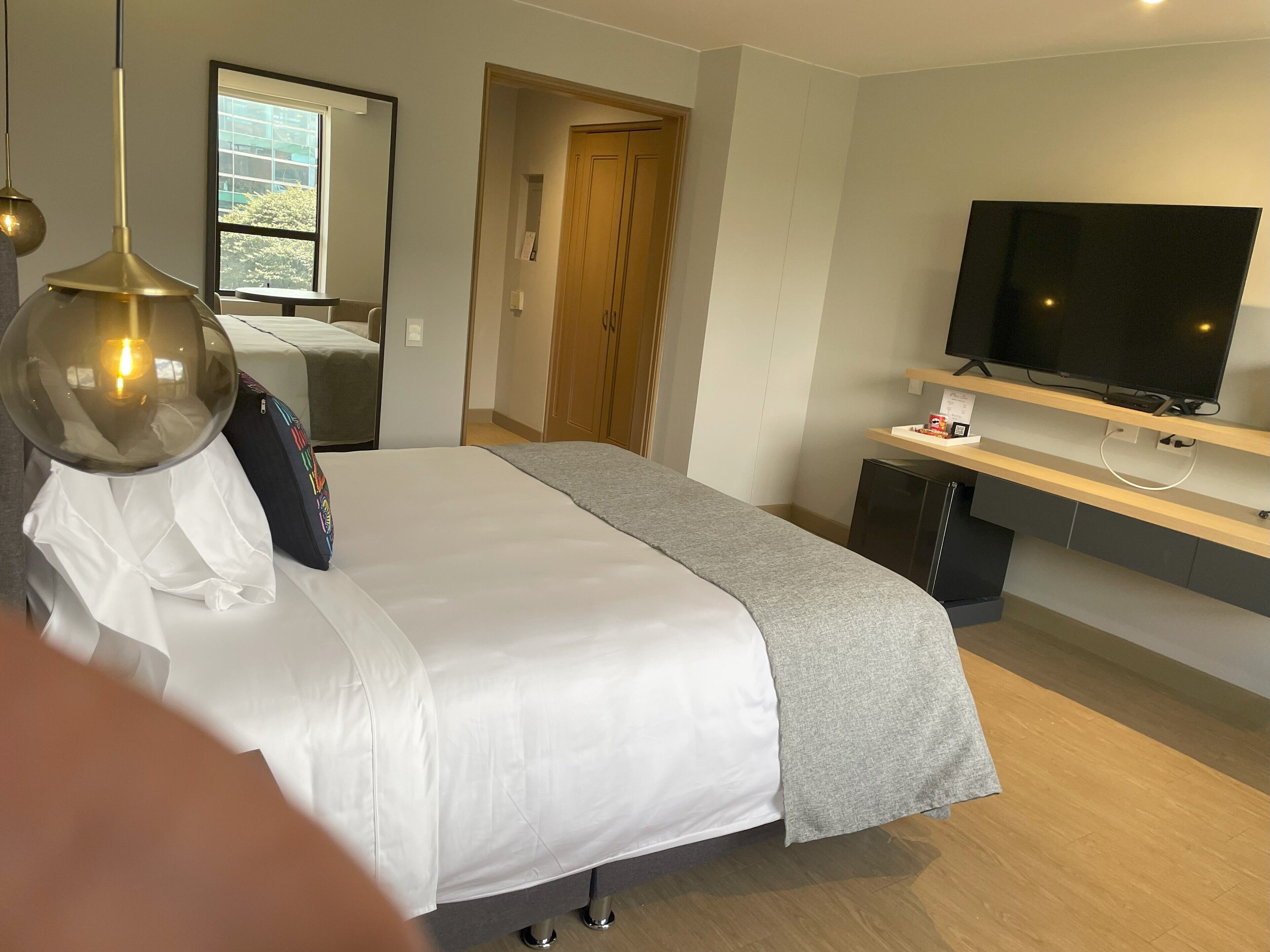 Camera d'albergo moderna con un ampio letto, una TV fissata a una mensola in legno e vista all'esterno attraverso una finestra.