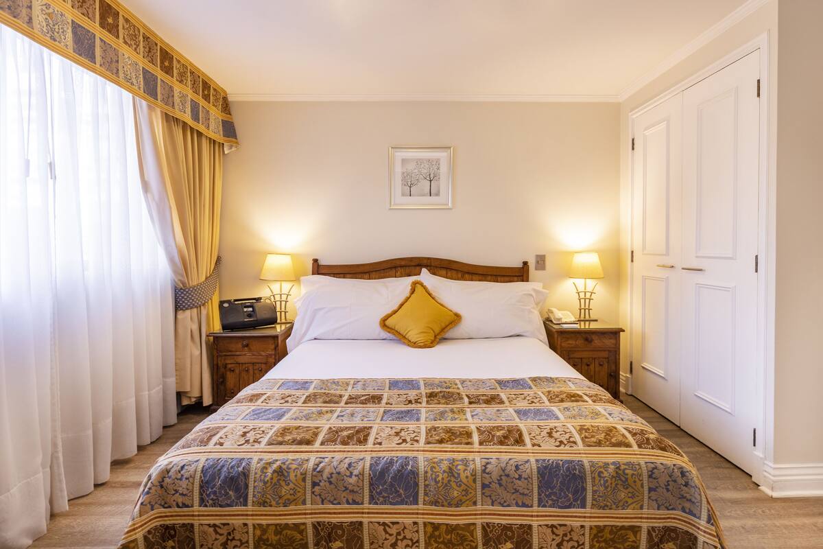 A neatly made bed with a patterned bedspread, two bedside lamps, and a framed picture on the wall.