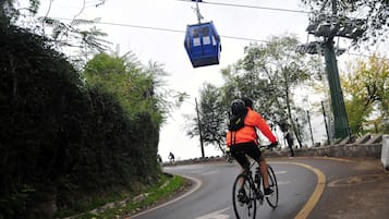 A cyclist on a road with a cable car overhead.