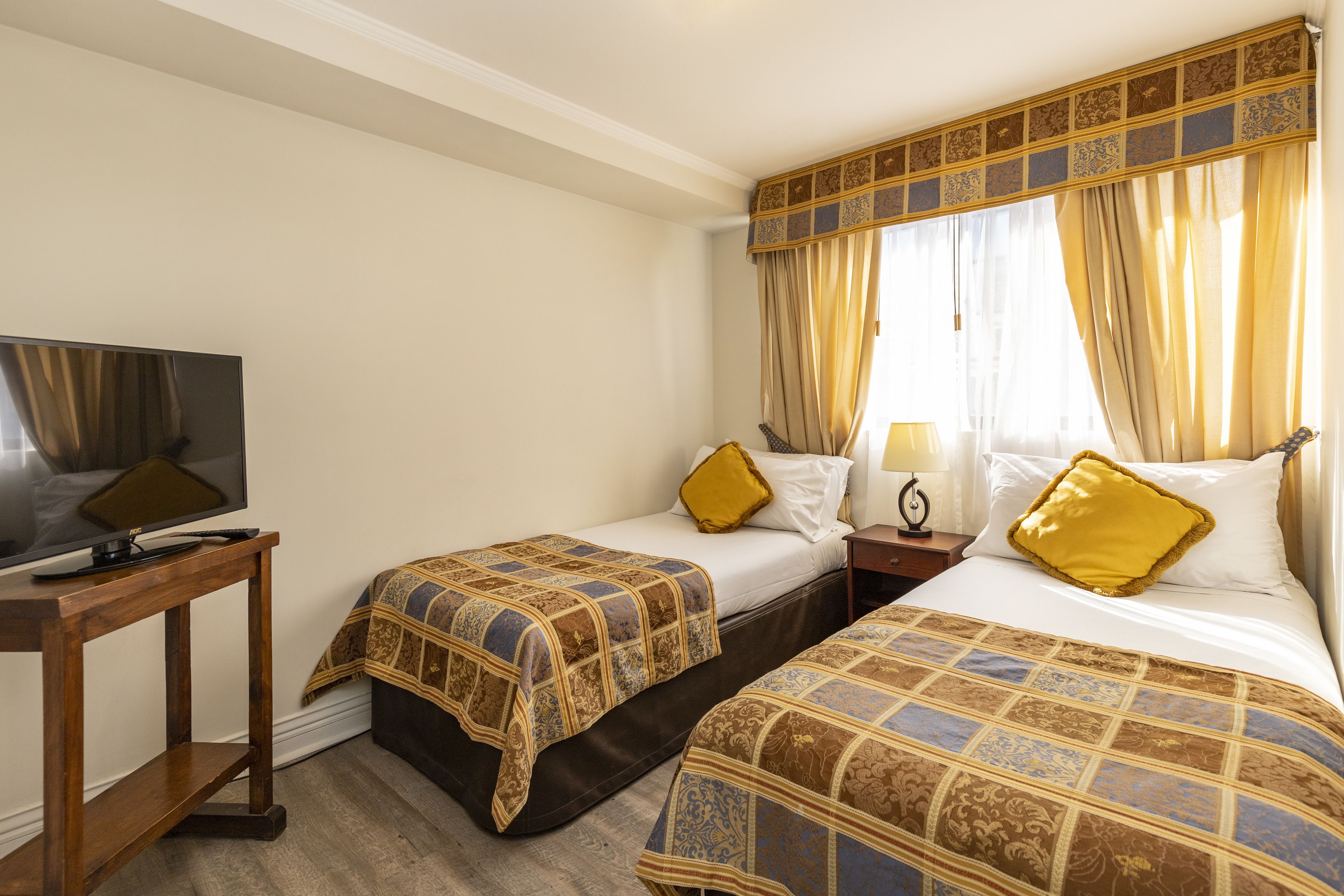 Habitación de hotel con dos camas, un televisor y una mesita de noche de madera.