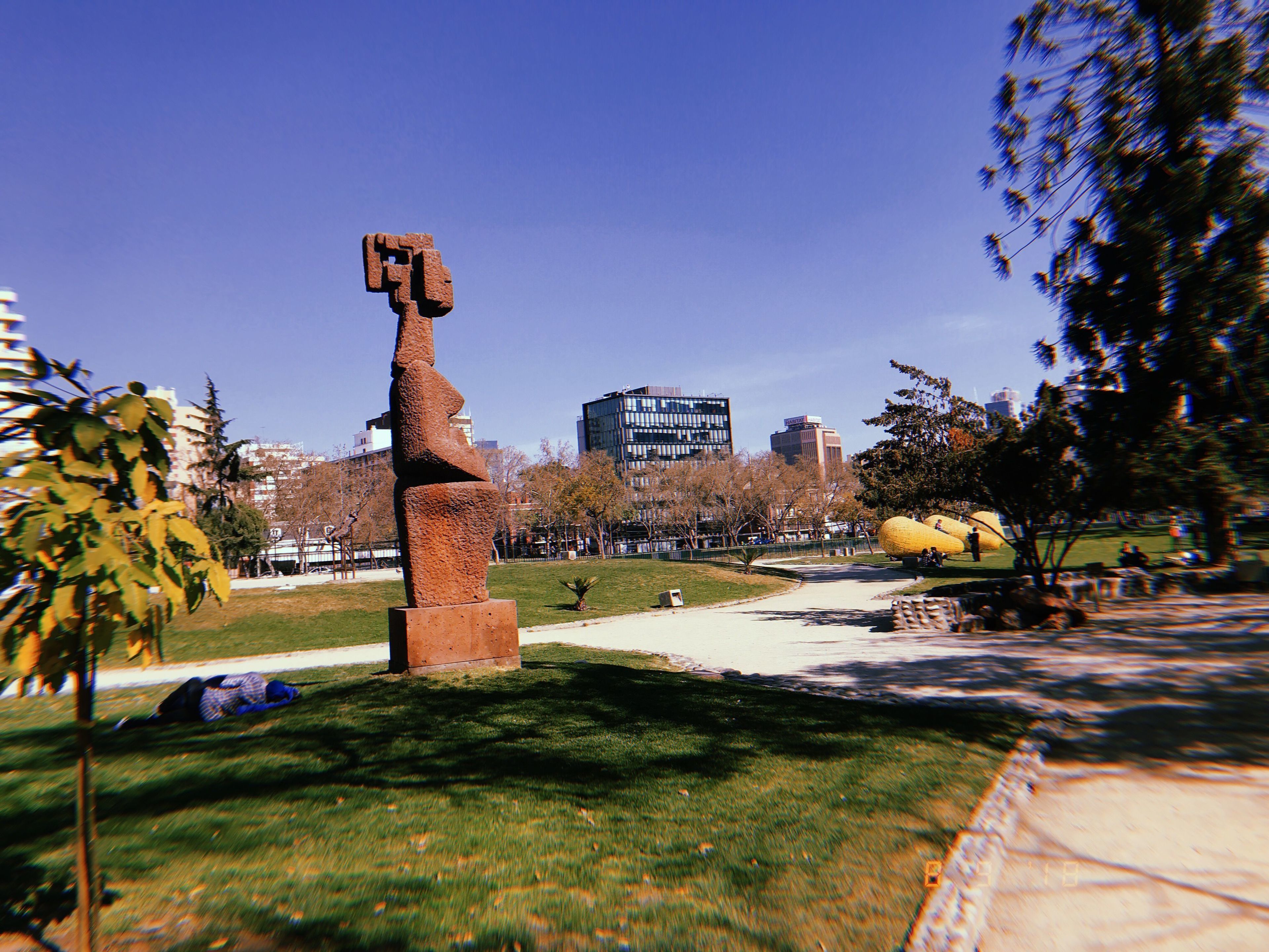 A sculpture in a park with a clear sky and buildings in the background.