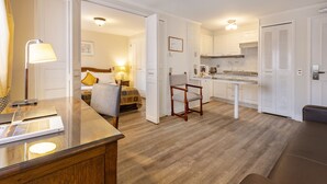 Una habitación de hotel moderna con piso de madera, un escritorio con lámpara, una silla, una cama con almohada amarilla y una kitchenette.