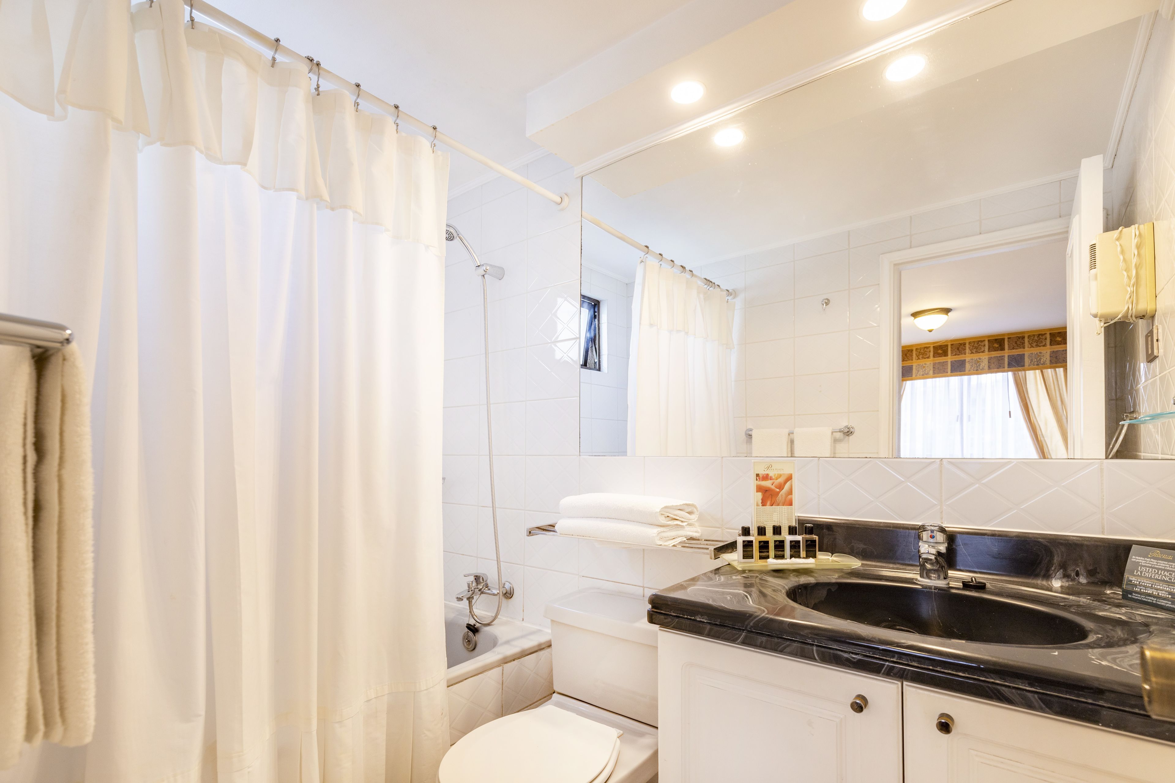 Een badkamer met douchegordijn, bad, toilet, wastafel met spiegel en handdoekrek.