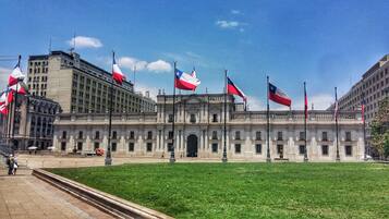 A large, historic building with multiple flags, a central entrance, and a surrounding green lawn.