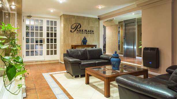 Una sala moderna con un sofá de cuero, una mesa de centro de vidrio y un jarrón decorativo. Hay un letrero de Park Plaza Apartments en la pared.