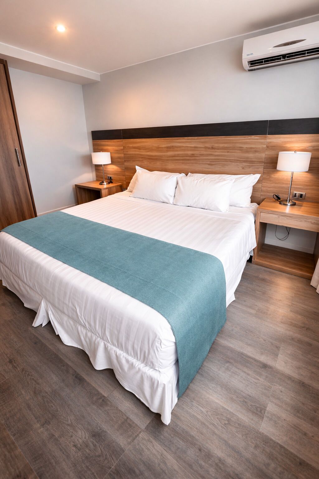 Habitación de hotel con una cama grande, cabecera de madera, dos mesitas de noche con lámparas y un equipo de aire acondicionado en la pared.
