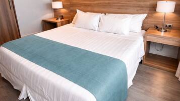 Habitación de hotel con una cama grande, cabecera de madera, dos mesitas de noche con lámparas y un equipo de aire acondicionado en la pared.