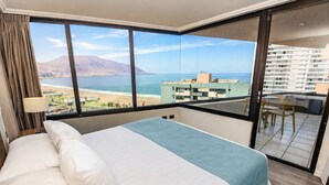 A hotel room with a large bed, a view of the sea, and a balcony with a table and chairs.