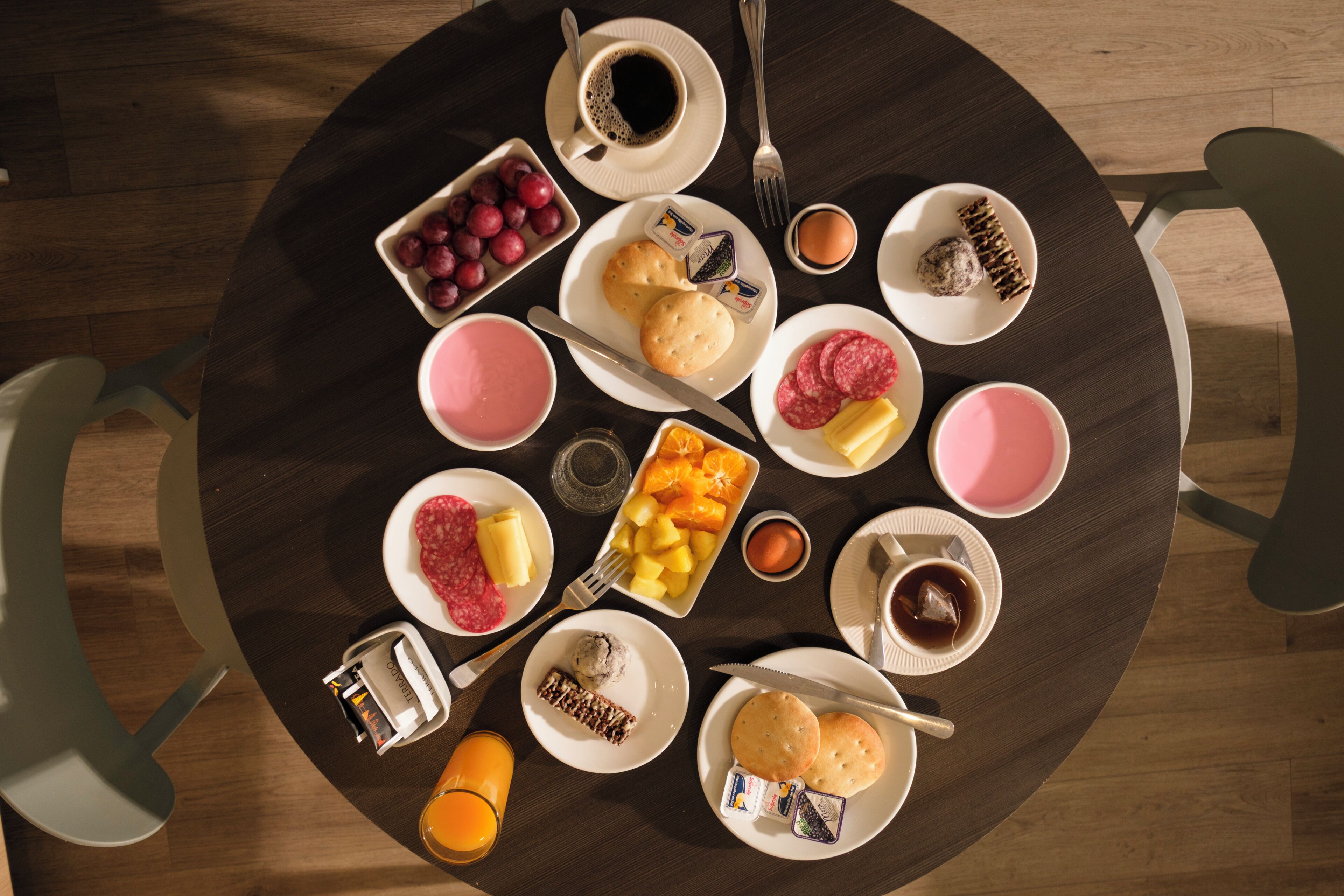 Une table de salle à manger ronde, sur laquelle sont disposés divers aliments pour le petit-déjeuner, notamment des fruits, des viennoiseries et des boissons.
