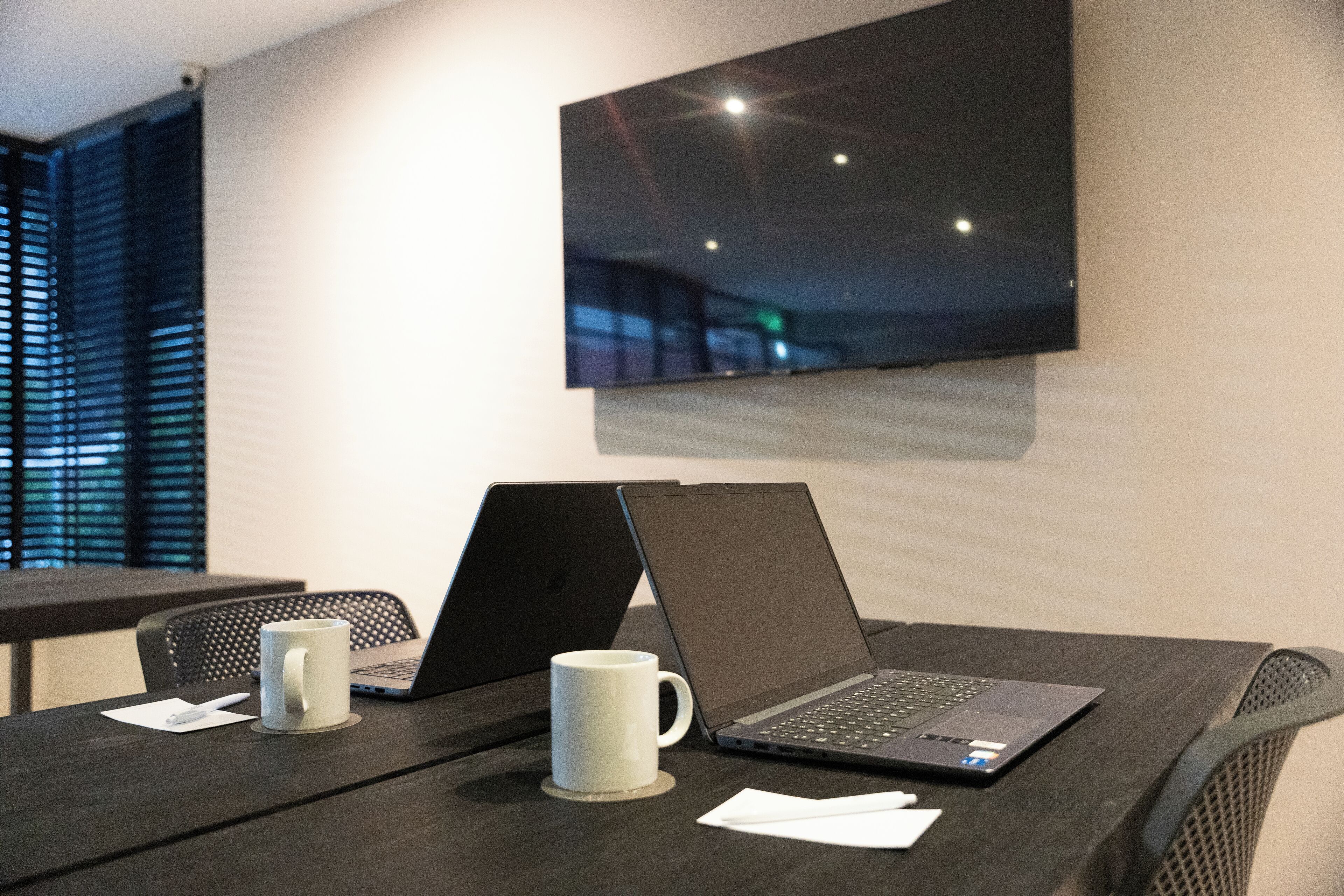 Un salón de conferencias con dos computadoras portátiles sobre una mesa, una taza blanca y documentos.