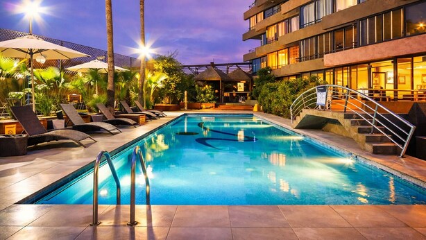 A swimming pool with lounge chairs, palm trees, and a building with balconies.