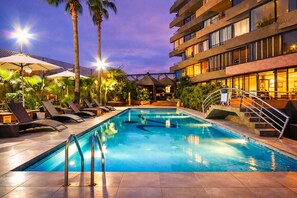 A swimming pool with lounge chairs, palm trees, and a building with balconies.