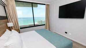 A hotel room with a large bed, a TV mounted on the wall, and a view of the ocean.