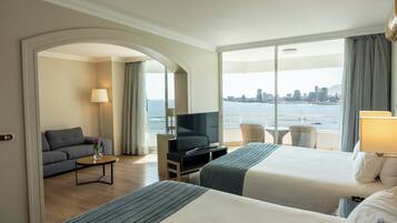 A hotel room with two beds, a TV, a sofa, a small table, and a view of the city and water.