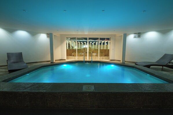 A swimming pool with two lounge chairs, a tiled floor, and a glass door leading to an outdoor area. - Terrado Suites Iquique (Iquique)