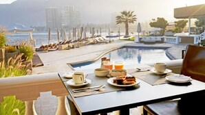 A poolside dining area with a view of the sea and mountains, lounge chairs, and a table set for breakfast. - Terrado Suites Iquique (Iquique)