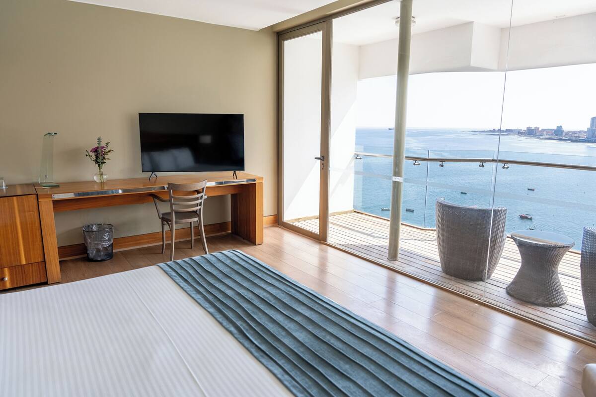 A modern hotel room with a balcony, a desk, a bed, and a TV.