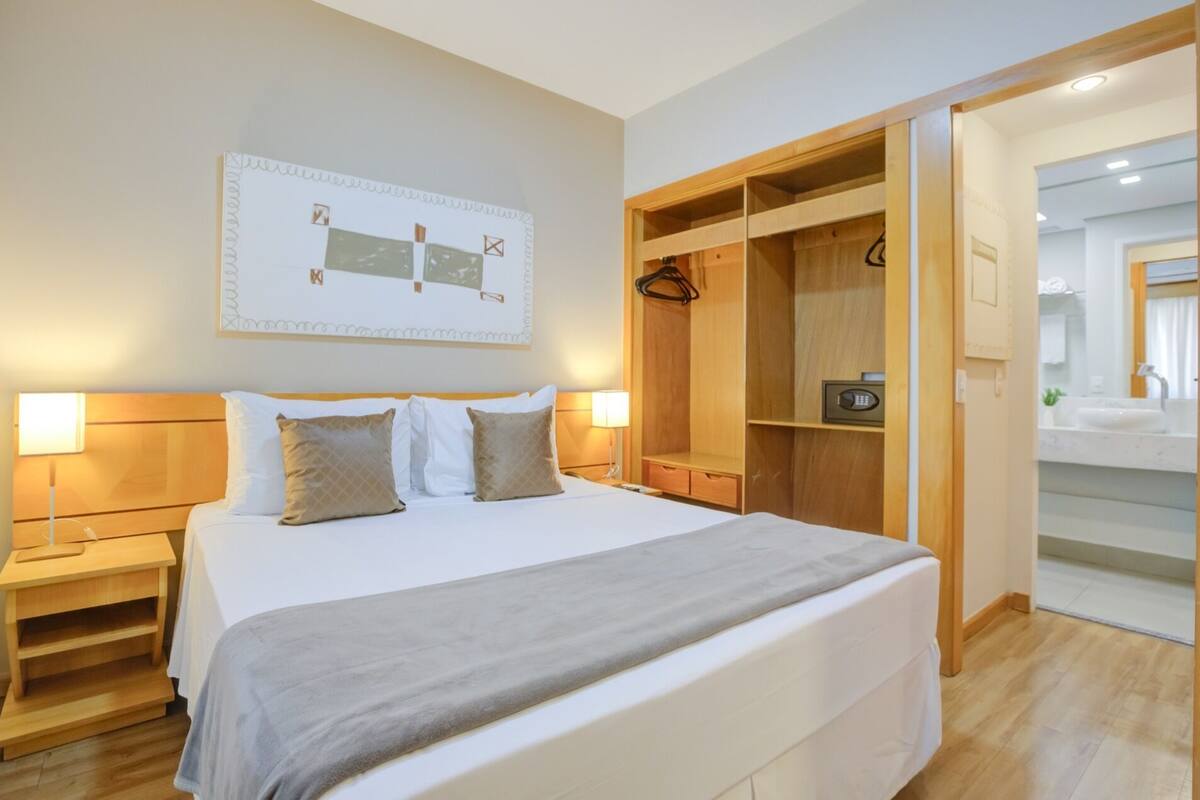 A hotel room with a large bed, bedside tables, a wardrobe, and a bathroom visible through an open door.