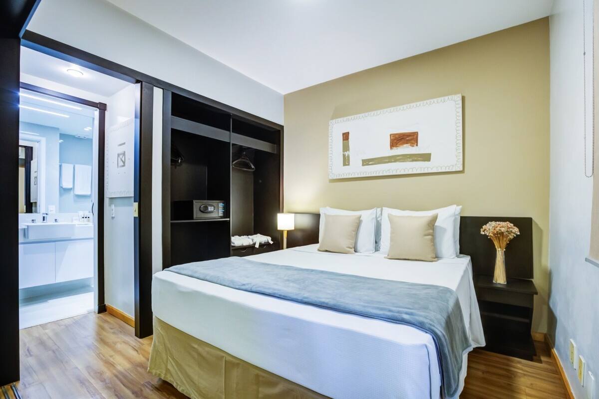 A hotel room with a bed, bedside table, lamp, and a painting on the wall.