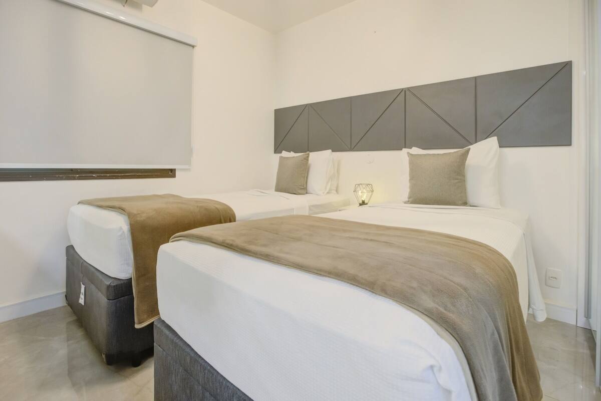 A hotel room with two beds, a grey headboard, and a bedside lamp.