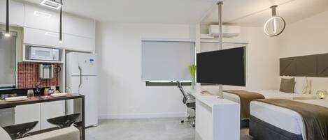 Une chambre d’hôtel moderne équipée d’une kitchenette, d’un téléviseur à écran plat, d’un lit et d’un bureau avec une chaise.