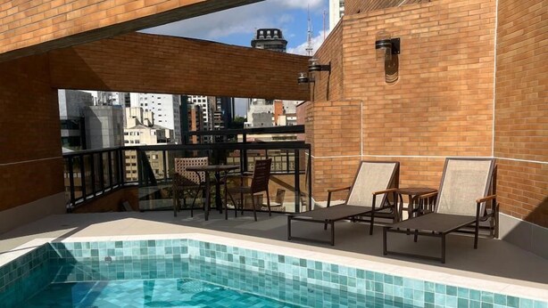 Un espace piscine aménagé sur le toit, avec une piscine carrelée, des chaises longues et un mur en briques.