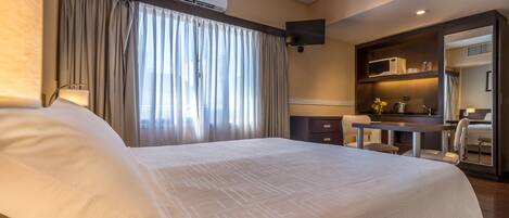 A hotel room with a large bed, a desk, a chair, a microwave, and a television.