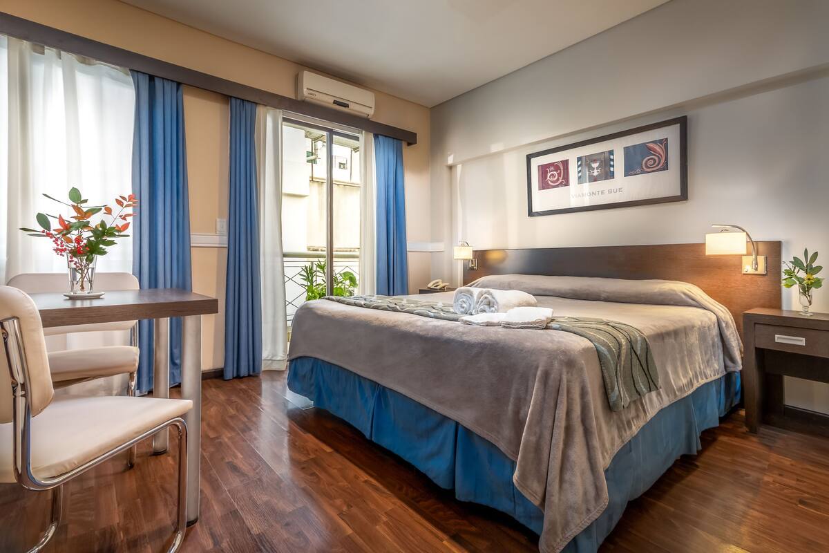 A hotel room with a bed, bedside table, chair, and a window with curtains.