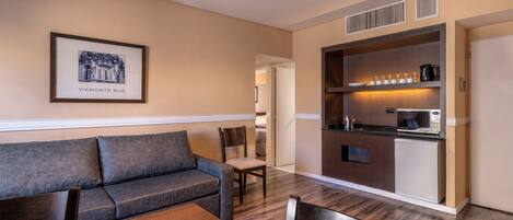 A modern hotel room with a sofa, dining table, and kitchenette.