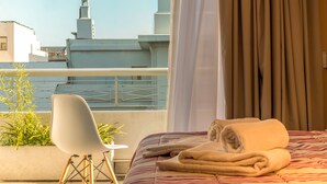 A hotel room with a bed, a chair, a potted plant, and a view of buildings. - Up Viamonte Hotel (Buenos Aires)