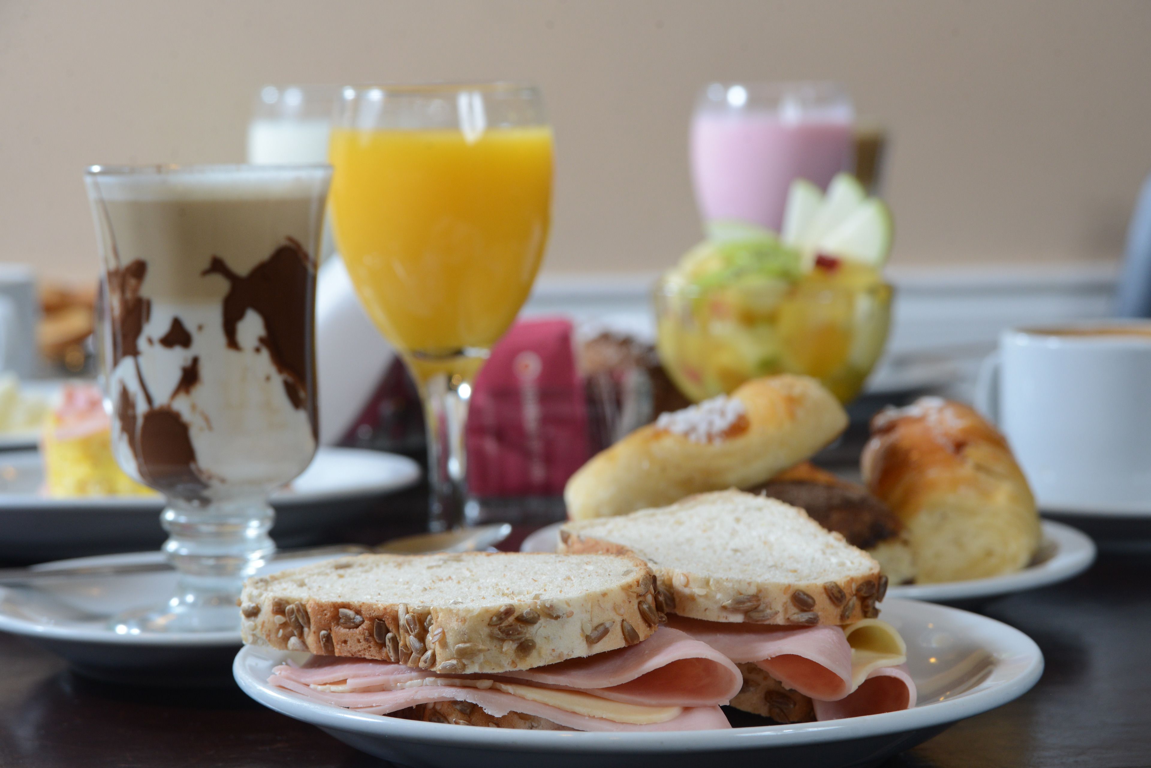 Una mesa con sándwiches, un vaso de zumo de naranja y un bol de fruta.