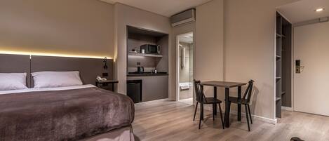 A modern hotel room with a large bed, a small kitchenette, a dining area with a table and chairs, and a separate bathroom.