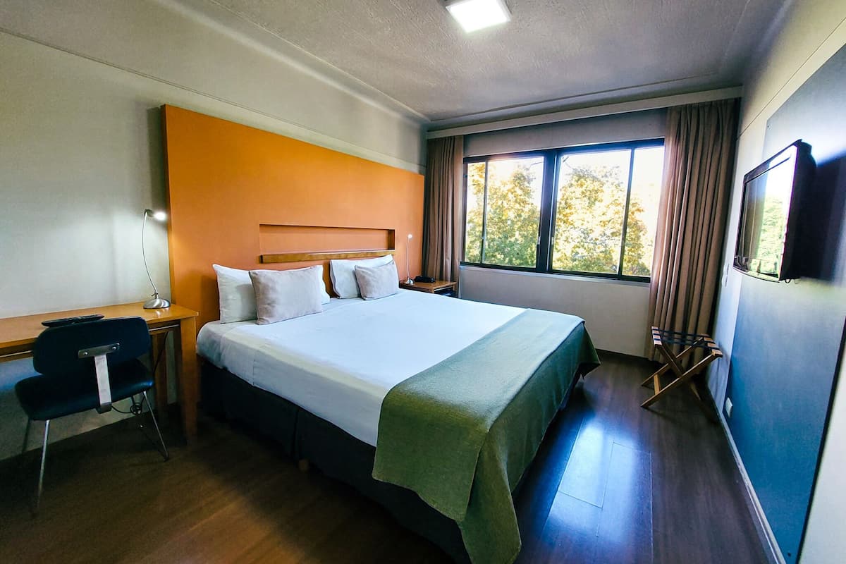 A hotel room with a bed, desk, chair, and a TV.
