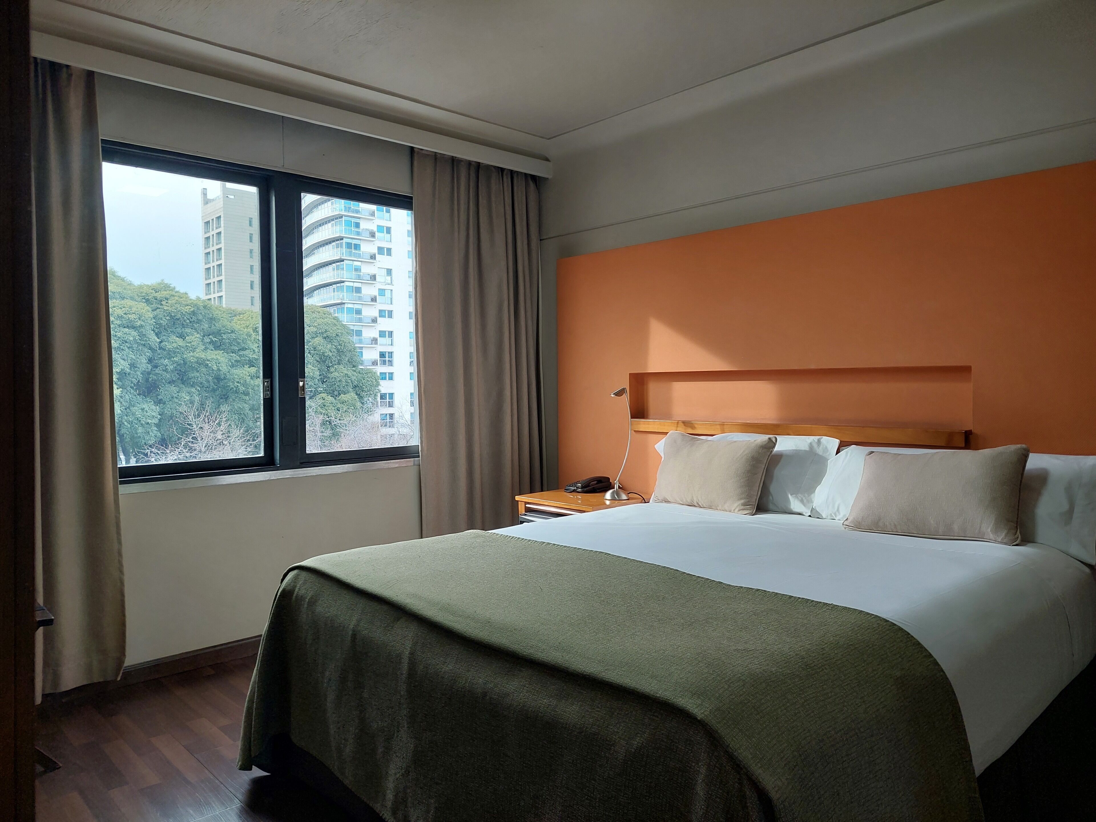Een hotelkamer met een groot bed, een nachtkastje met een lamp en een raam met gordijnen.