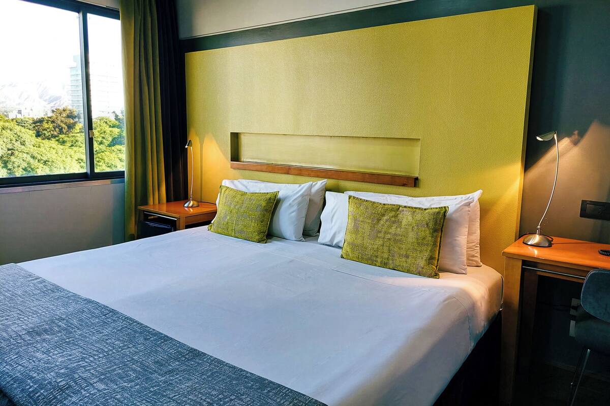 A hotel room with a large bed, two bedside tables, a nightstand, a desk, and a chair.