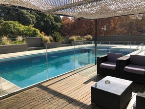 A rooftop pool area with clear glass railings, wooden decking, and modern outdoor furniture. - Raices Aconcagua Mendoza (Mendoza)