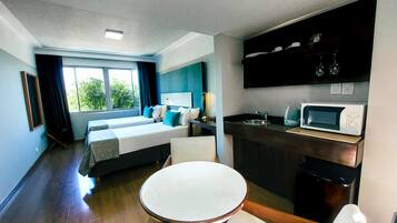 Una habitación de hotel con cama, una mesa redonda, una kitchenette con microondas y una ventana con cortinas.