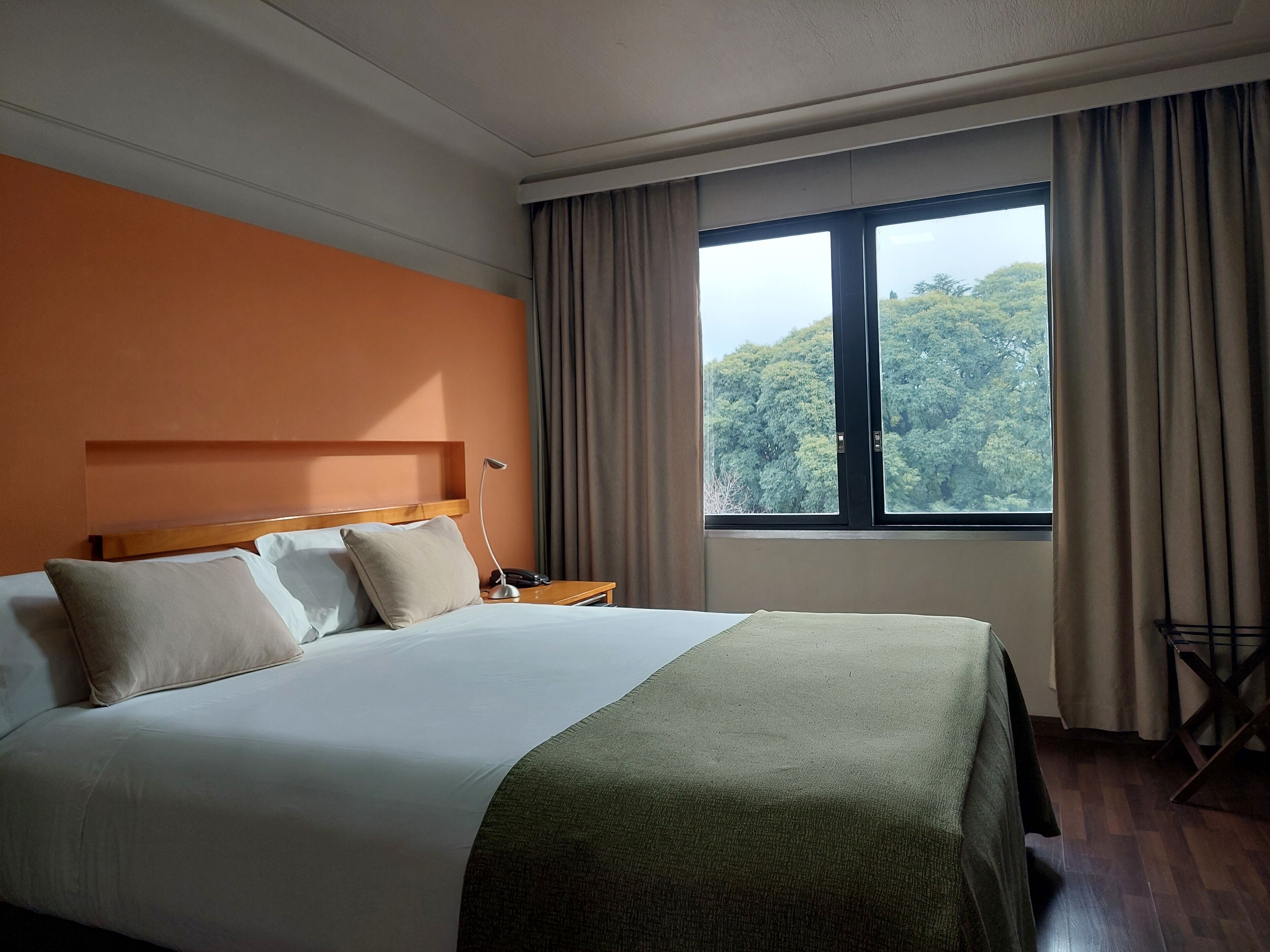 A hotel room with a large bed, a bedside table with a lamp, and a window with curtains.