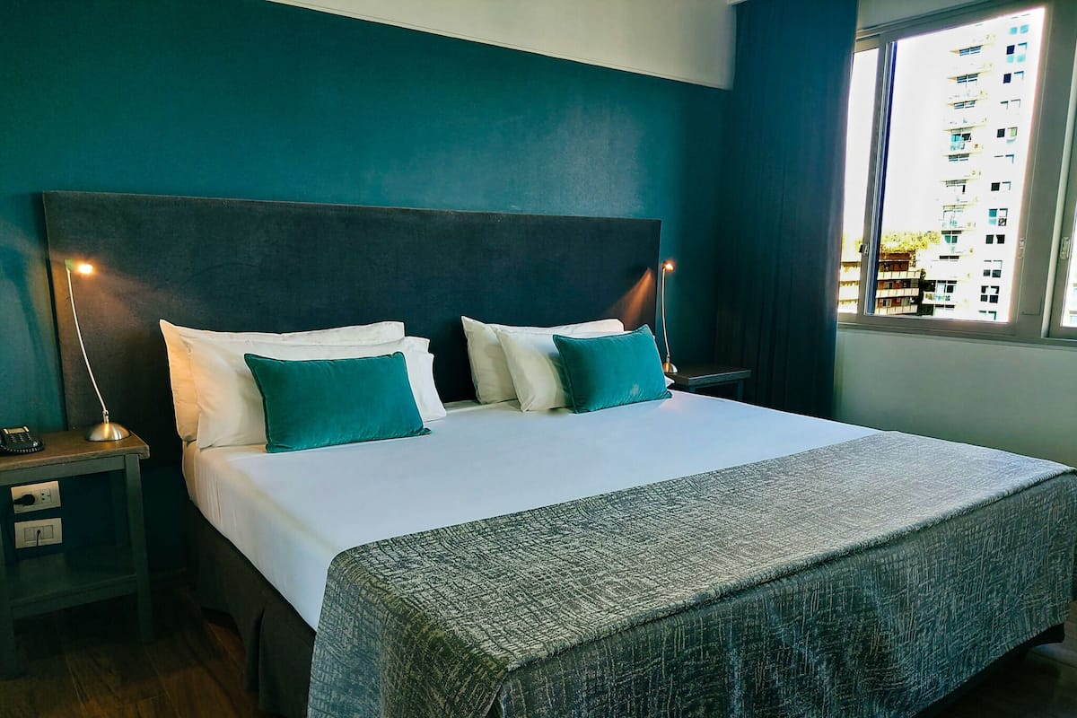 A hotel room with a large bed, two bedside tables with lamps, and a view of buildings through the window.