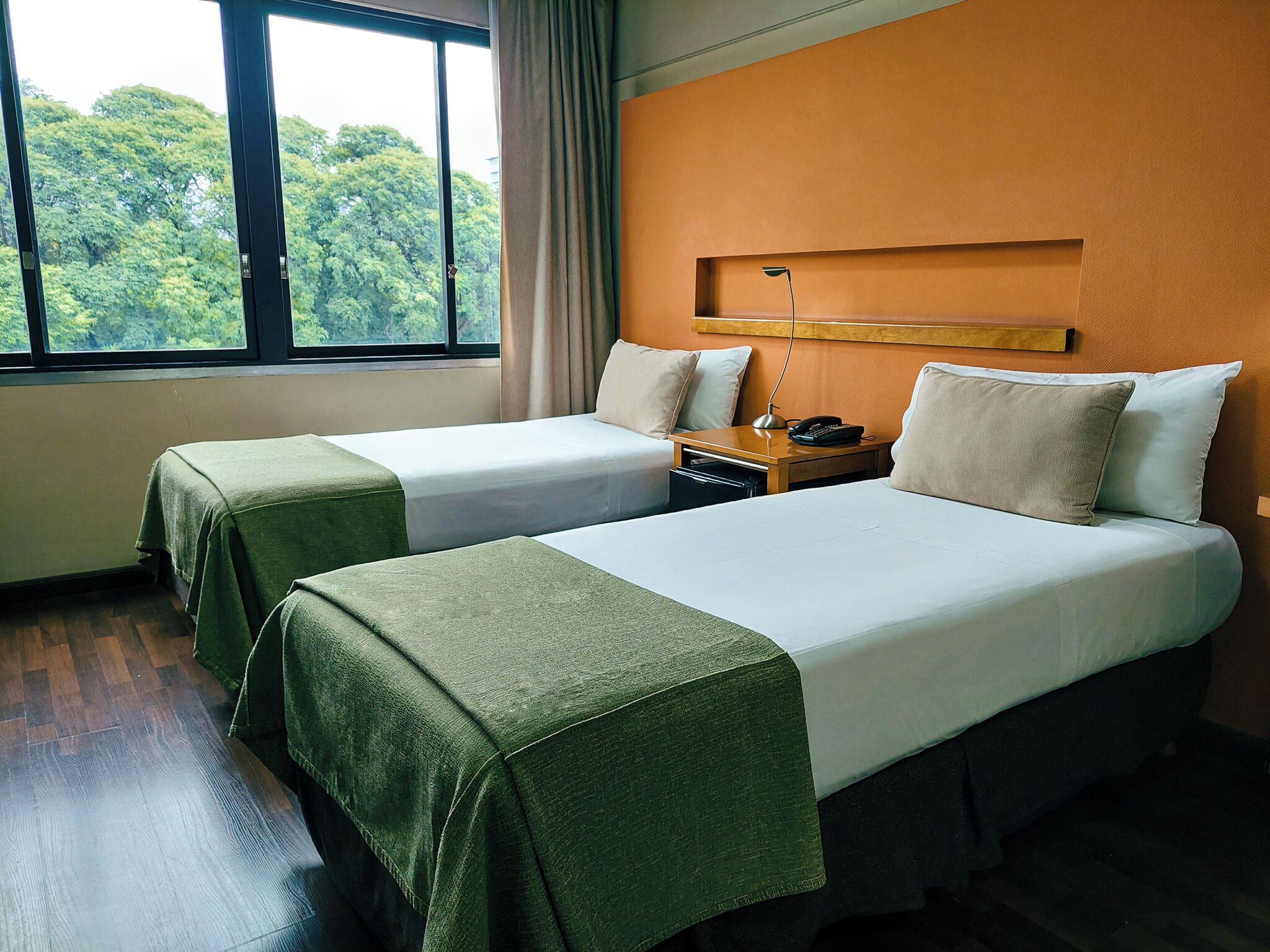 Une chambre d’hôtel avec deux lits, une table de chevet, une lampe et une vue sur la verdure par la fenêtre.