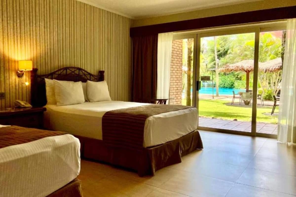 A hotel room with two beds, a large sliding glass door to a pool area, and a brick wall.