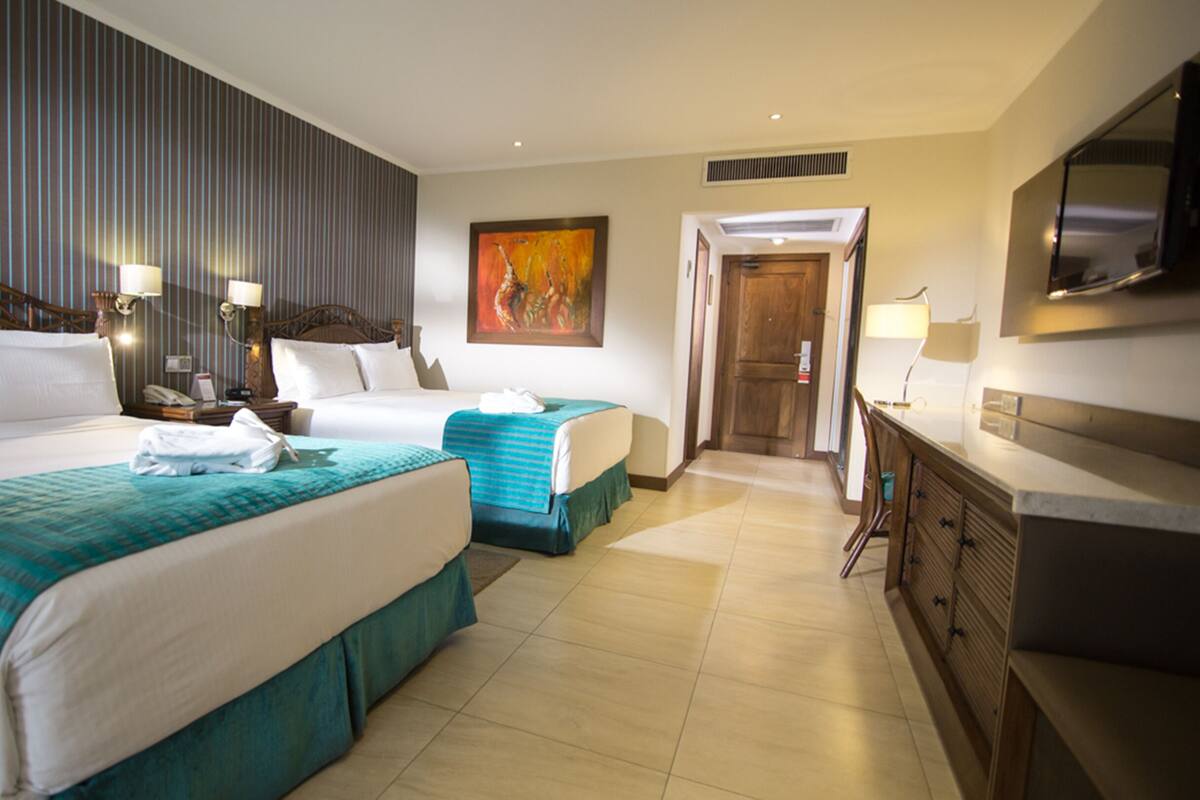 A hotel room with two beds, a desk, a TV, and a painting on the wall.