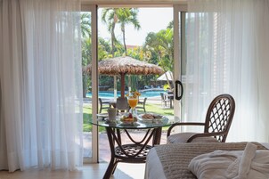 Una habitación con una mesa y sillas de vidrio, una cama y vistas a una piscina y vegetación tropical.