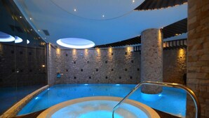 Un bain à remous doté d’une terrasse en bois et de murs en pierre, entouré d’une piscine.