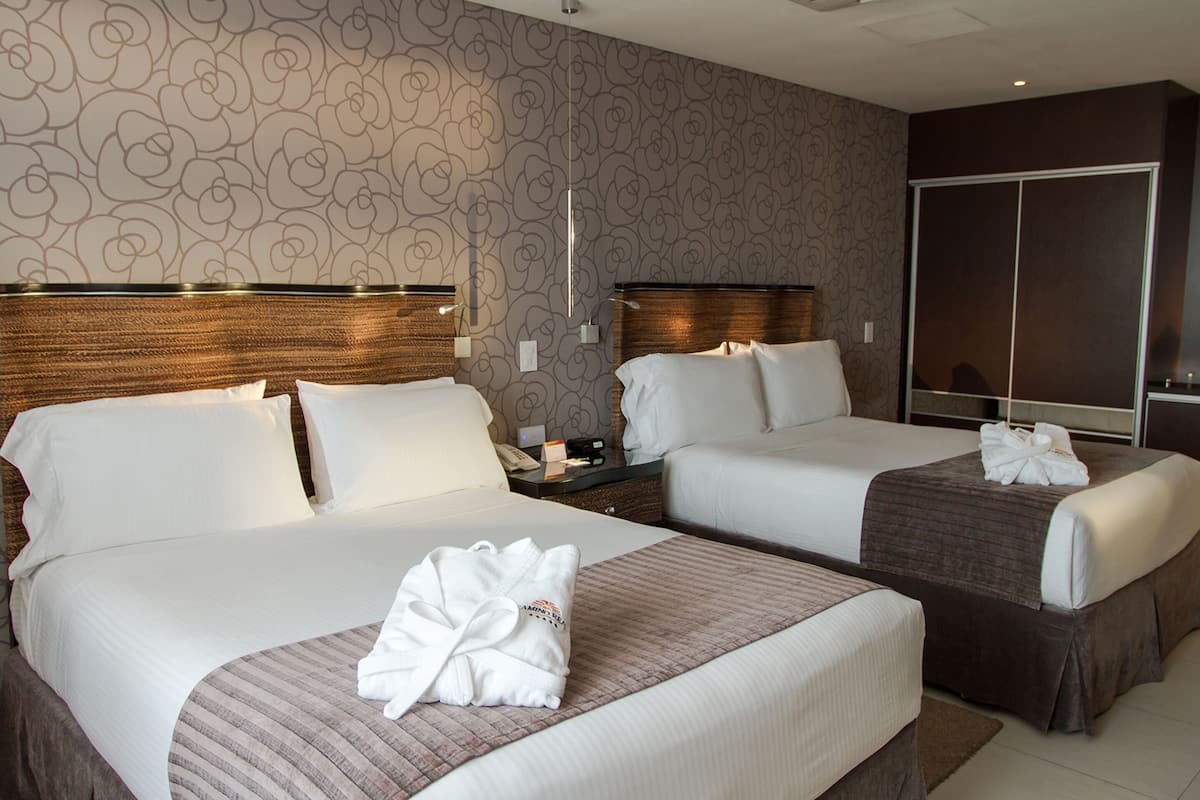 A hotel room with two beds, a wardrobe, and a nightstand with a lamp.