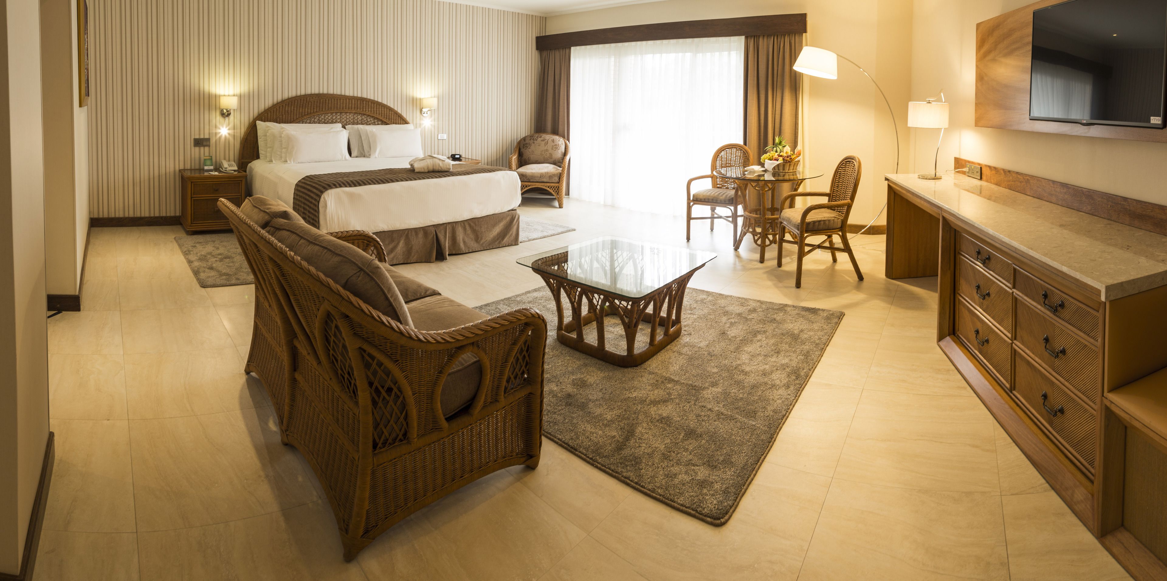Une chambre d’hôtel avec un grand lit, un canapé, une table à manger avec des chaises, une télévision et un bureau avec des tiroirs.